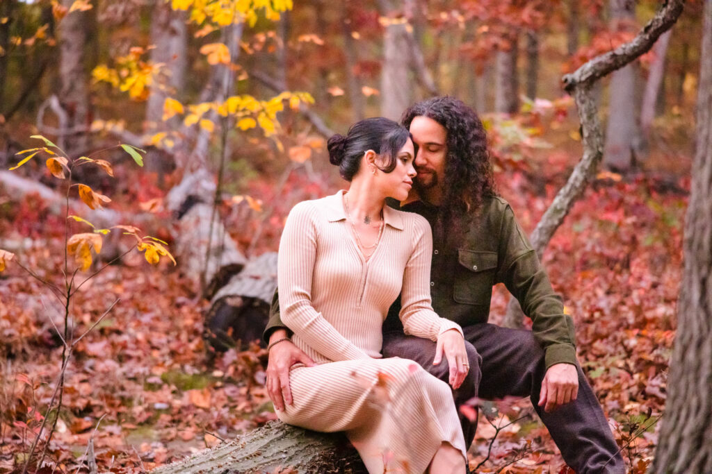 Couple sharing an intimate moment seated on a log in a colorful autumn forest during their engagement session.
