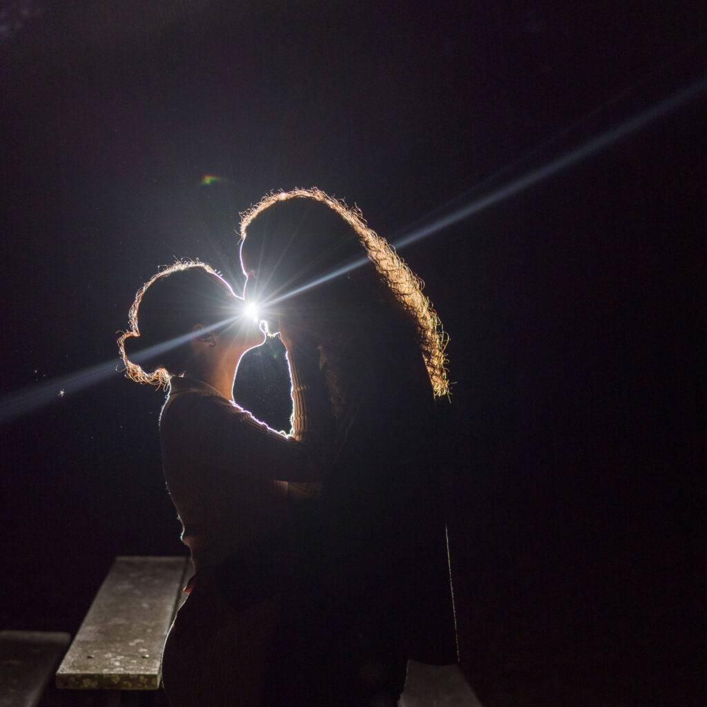 Silhouetted couple sharing a kiss under dramatic backlighting during their fall engagement session.