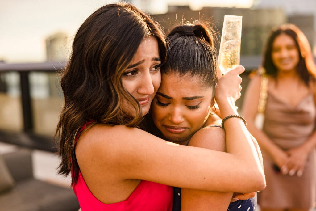 Two women embrace in an emotional, tearful hug after a rooftop proposal, capturing the raw joy and heartfelt connection of the moment in golden sunlight.
