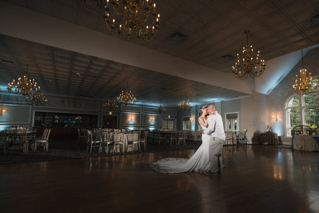 Bride and groom share an intimate, cinematic first dance under glowing chandeliers in an empty ballroom, dramatically lit to highlight the emotion and atmosphere of the moment.