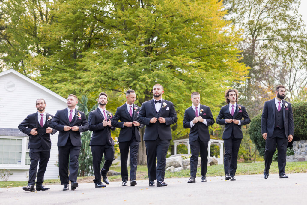 Groomsmen walking confidently outdoors in matching black suits and burgundy ties, featuring classic men’s wedding party portrait photography.
