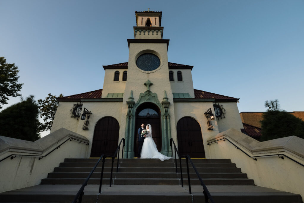 Bride and groom standing on the front steps of a grand historic church at sunset, showcasing timeless wedding portraiture and architectural elegance.