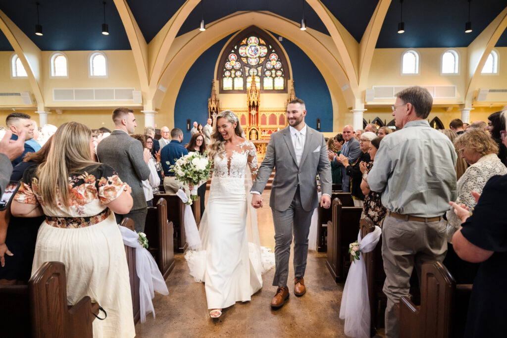 Bride and groom walking back up the aisle of a bright stained-glass church as guests cheer, highlighting candid documentary-style wedding photography, perfect for couples exploring the best platforms to compare wedding photographers.