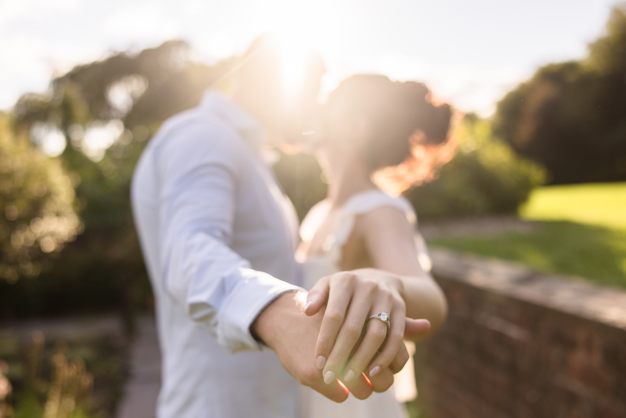 Engagement photo with a close-up of the bride’s engagement ring as the couple kisses in soft golden sunlight, capturing a dreamy and romantic photography style.