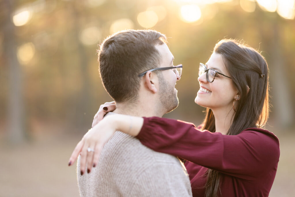 Bride-to-be smiling with her arms wrapped around her fiancé during golden hour.