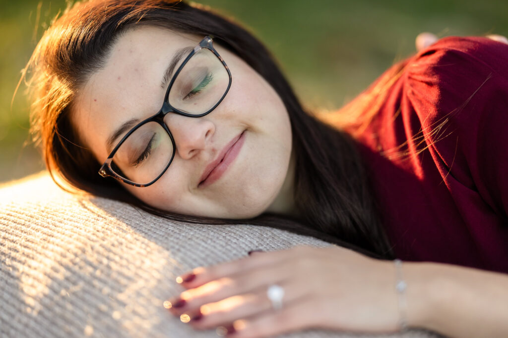 Close-up of bride-to-be resting peacefully on her fiancé’s shoulder, engagement ring in focus, during golden hour.