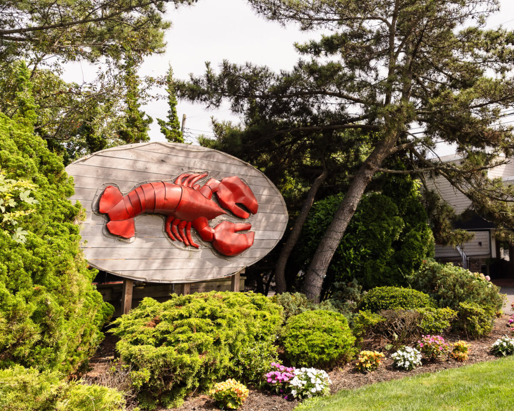 Iconic red lobster sign at The Snapper Inn surrounded by lush greenery and garden flowers on the Oakdale waterfront.
