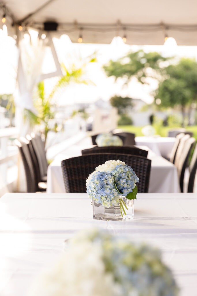 Soft blue and white hydrangea centerpiece in a glass vase decorating an outdoor reception table at The Snapper Inn overlooking the marina.