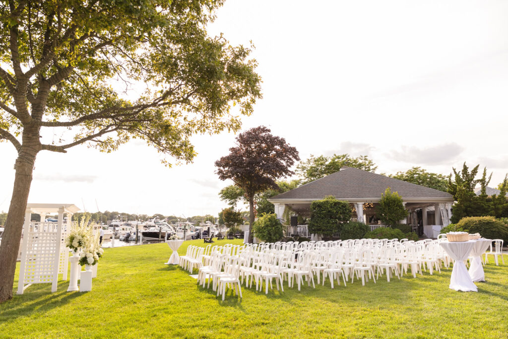 Outdoor waterfront ceremony setup on the lawn at The Snapper Inn, featuring rows of white chairs, floral décor, and marina views at sunset.