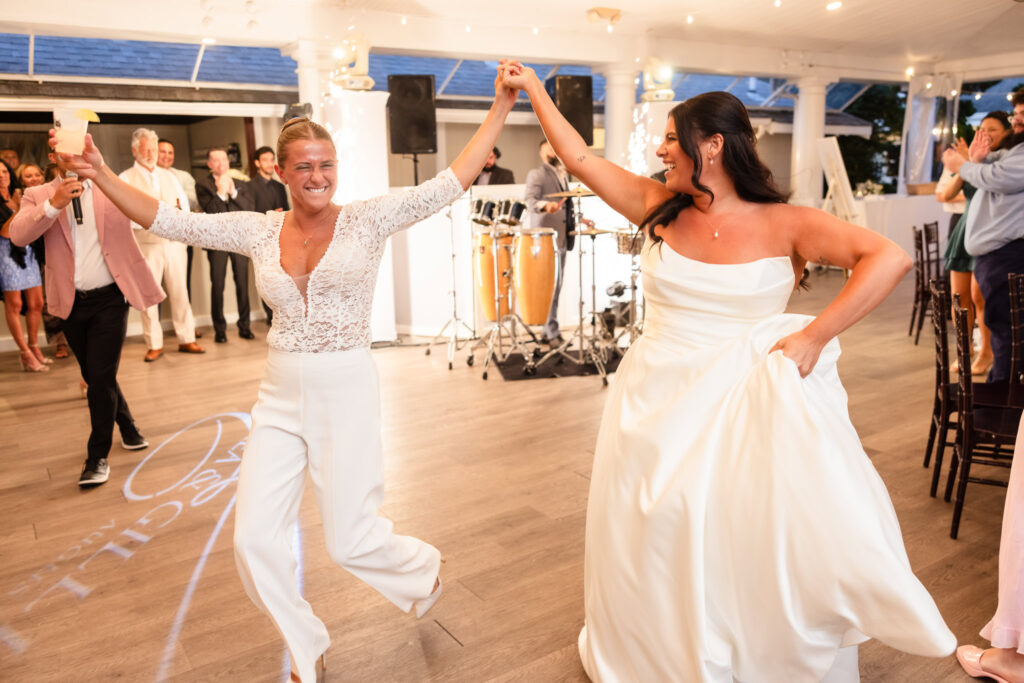 Brides joyfully entering their wedding reception hand in hand, celebrating with guests on the dance floor.