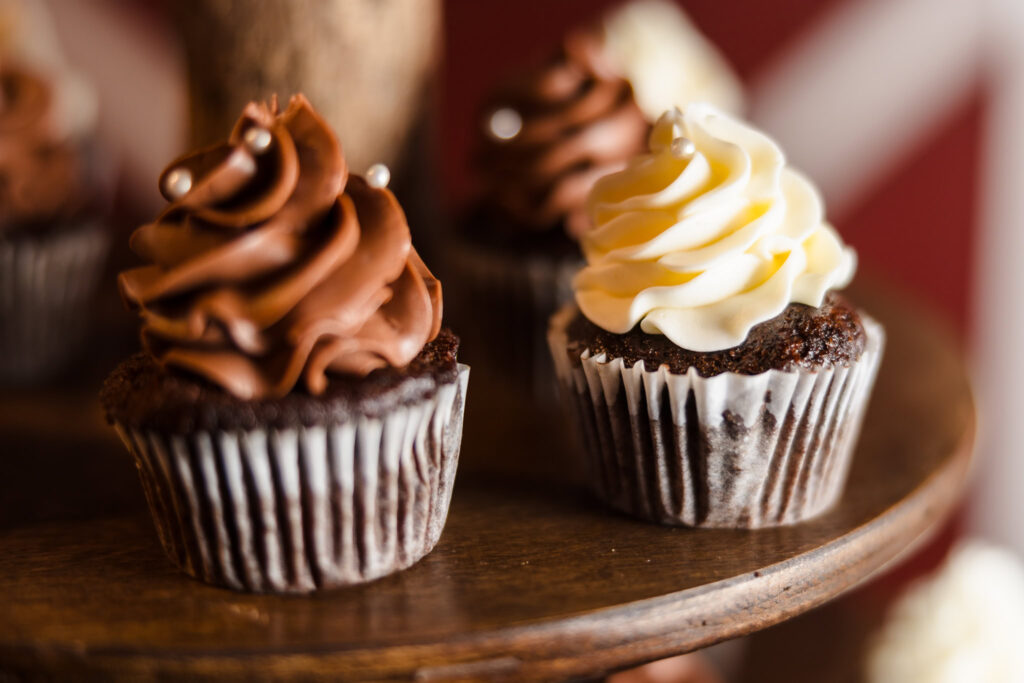 Close-up of chocolate cupcakes with swirls of chocolate and vanilla frosting, topped with pearl sprinkles, displayed on a rustic wooden dessert stand at the wedding reception.