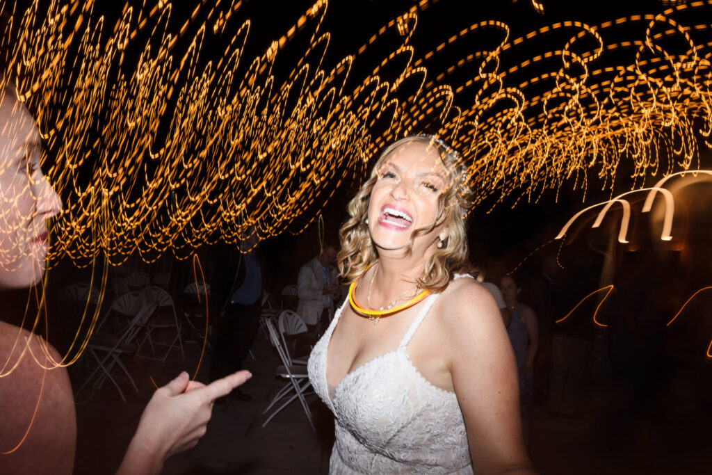 Bride laughing joyfully under swirling bistro lights during the evening dance party at her wedding reception.