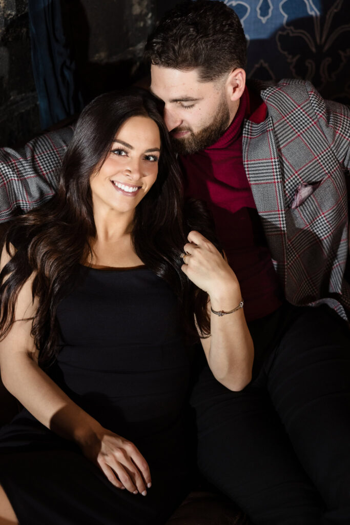 Bride-to-be smiles while resting against her fiancé, capturing warmth and vintage romance on Long Island.