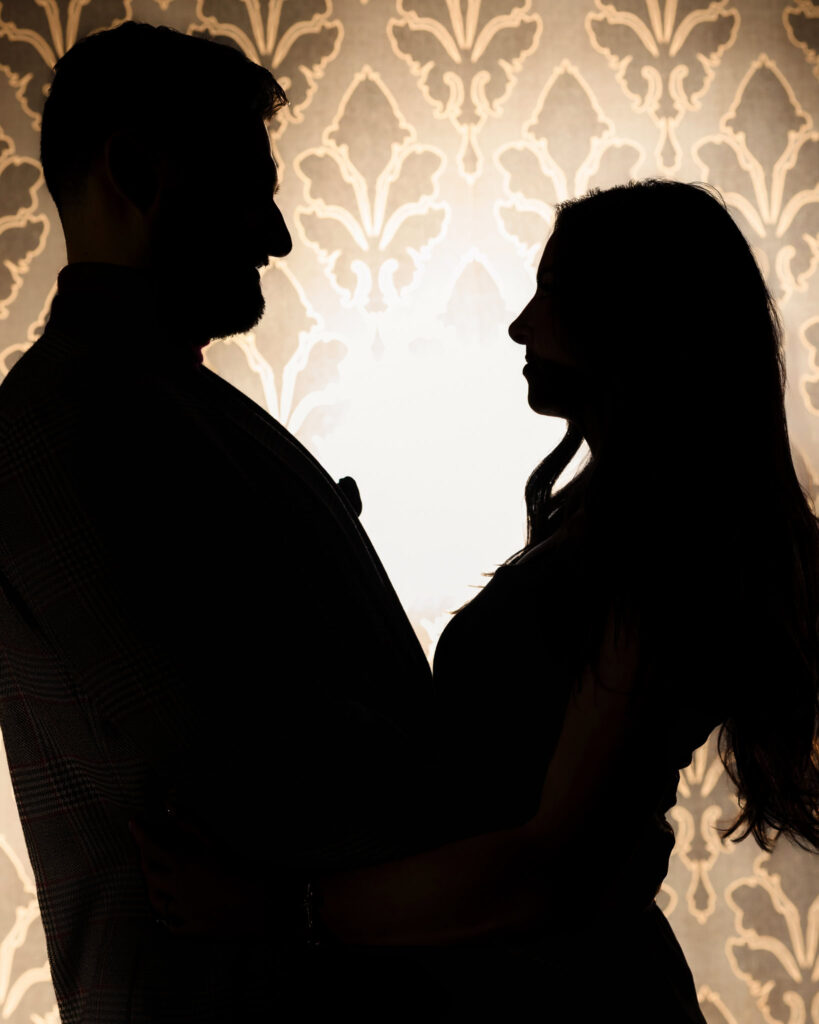 Silhouette of engaged couple facing each other against vintage wallpaper, evoking moody romance.
