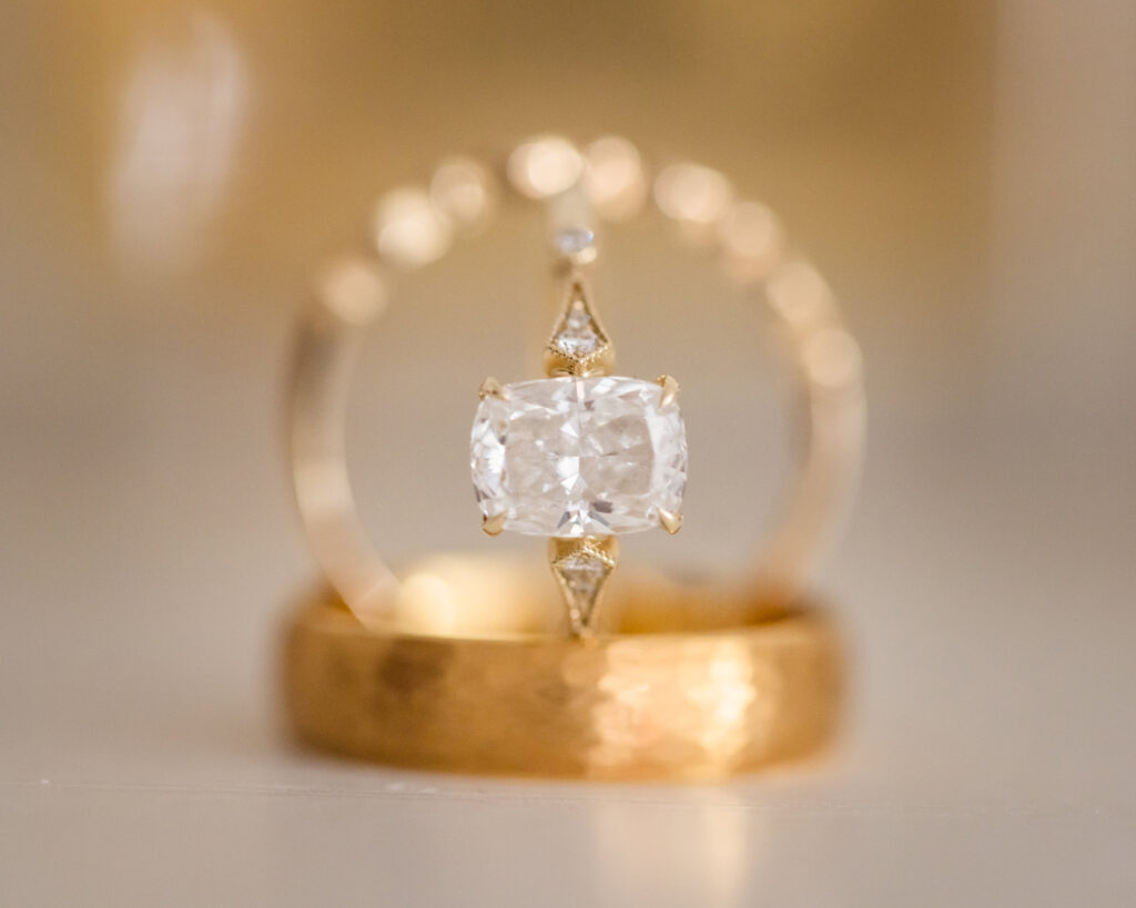 Close-up of elegant cushion-cut diamond engagement ring and gold wedding bands from a wedding.