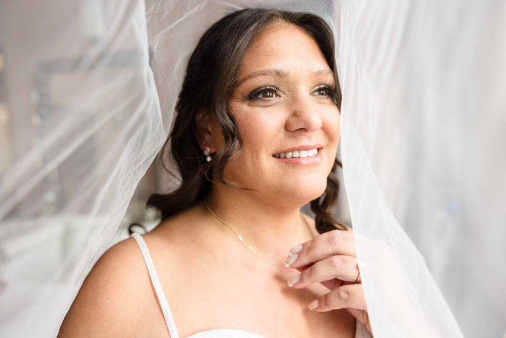 Bride smiles softly beneath her veil in a glowing bridal portrait before her fall wedding at Gatsby on the Ocean.
