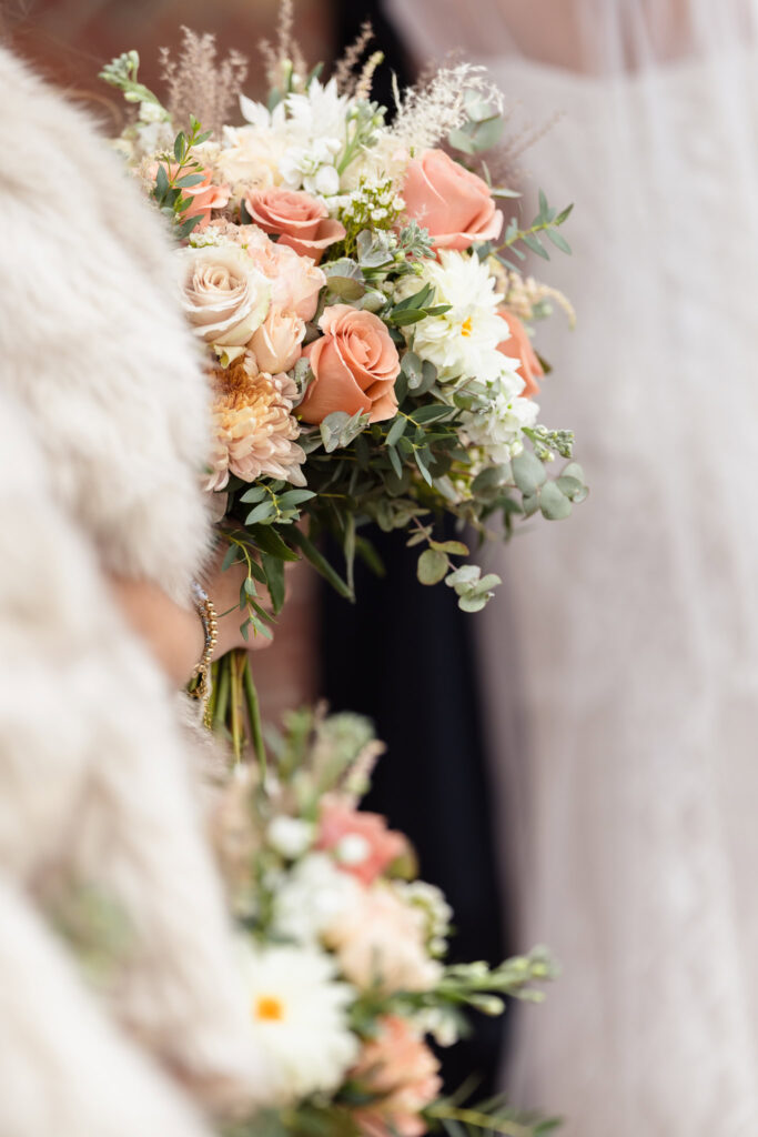 Close-up of fall wedding bouquet with peach roses, white dahlias, and greenery held by the bride at Gatsby on the Ocean.