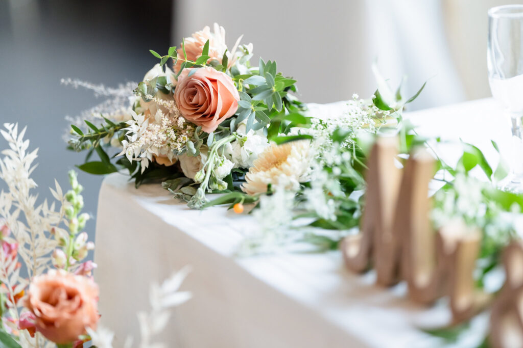 Soft peach and ivory floral arrangement with greenery decorates the sweetheart table at a fall wedding reception at Gatsby on the Ocean.
