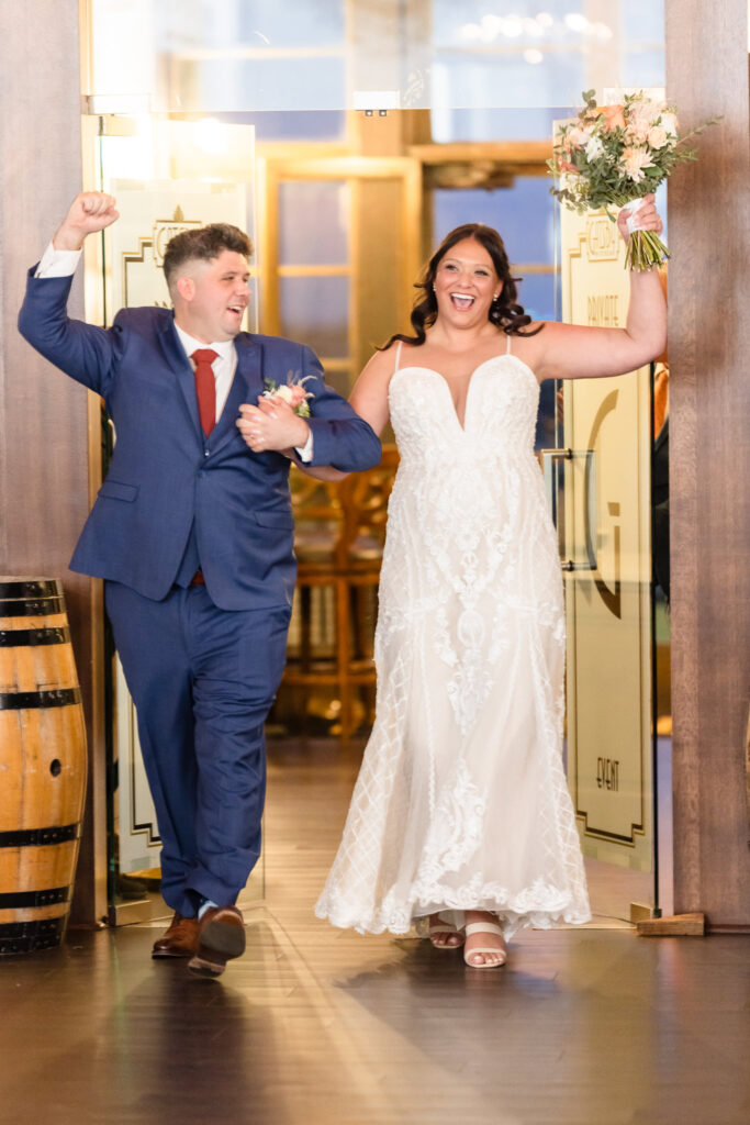 Bride and groom make a joyful grand entrance into their wedding reception at Gatsby on the Ocean, celebrating with raised hands and big smiles.