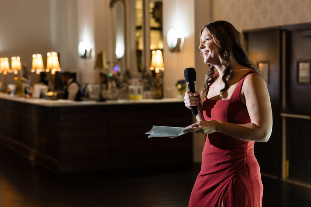 Bridesmaid in a rust-colored dress delivers a heartfelt speech during the fall wedding reception at Gatsby on the Ocean.