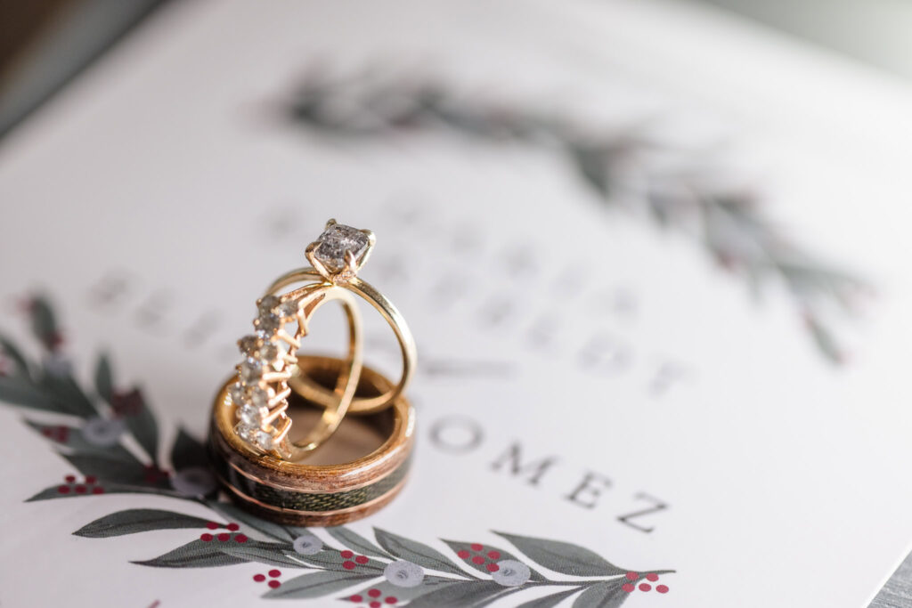 Close-up of gold engagement ring and wedding bands with diamonds, styled on a botanical wedding invitation at Giorgio’s Baiting Hollow.