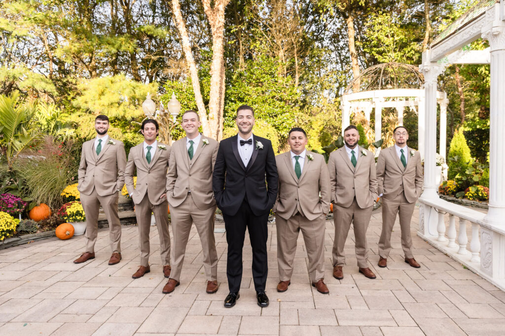 Groom with groomsmen in tan suits and green ties posing in the garden courtyard at Giorgio’s Baiting Hollow surrounded by fall decor.