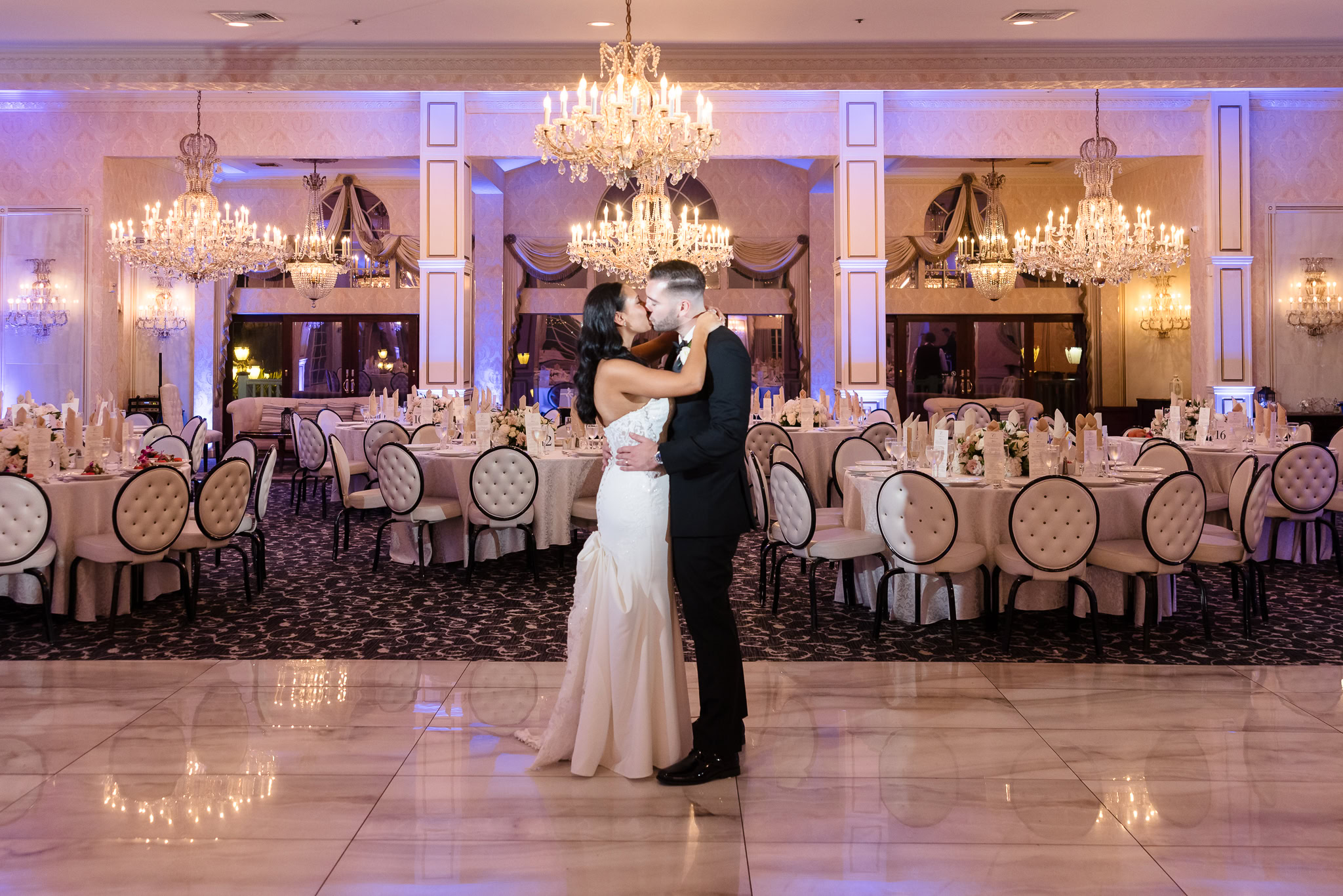 Bride and groom sharing a kiss in the center of Giorgio’s Baiting Hollow’s grand ballroom, surrounded by elegant chandeliers and set tables.