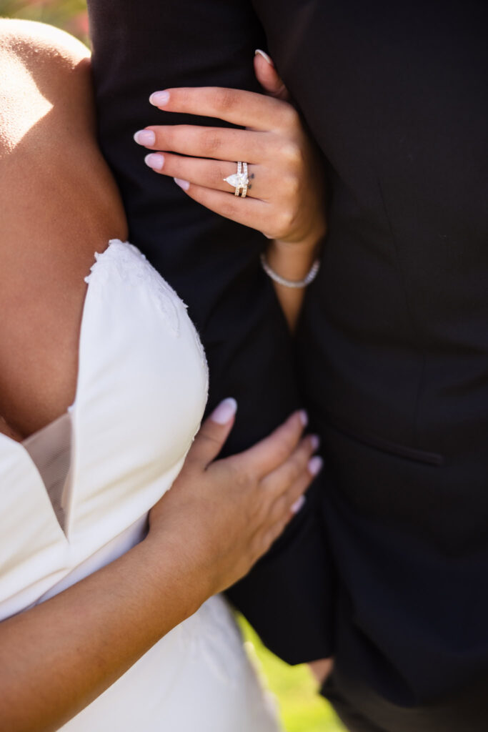 Close-up of bride AnnaLisa’s hand resting on her groom’s arm, showcasing her gold wedding band and pear-shaped diamond engagement ring during their wedding.