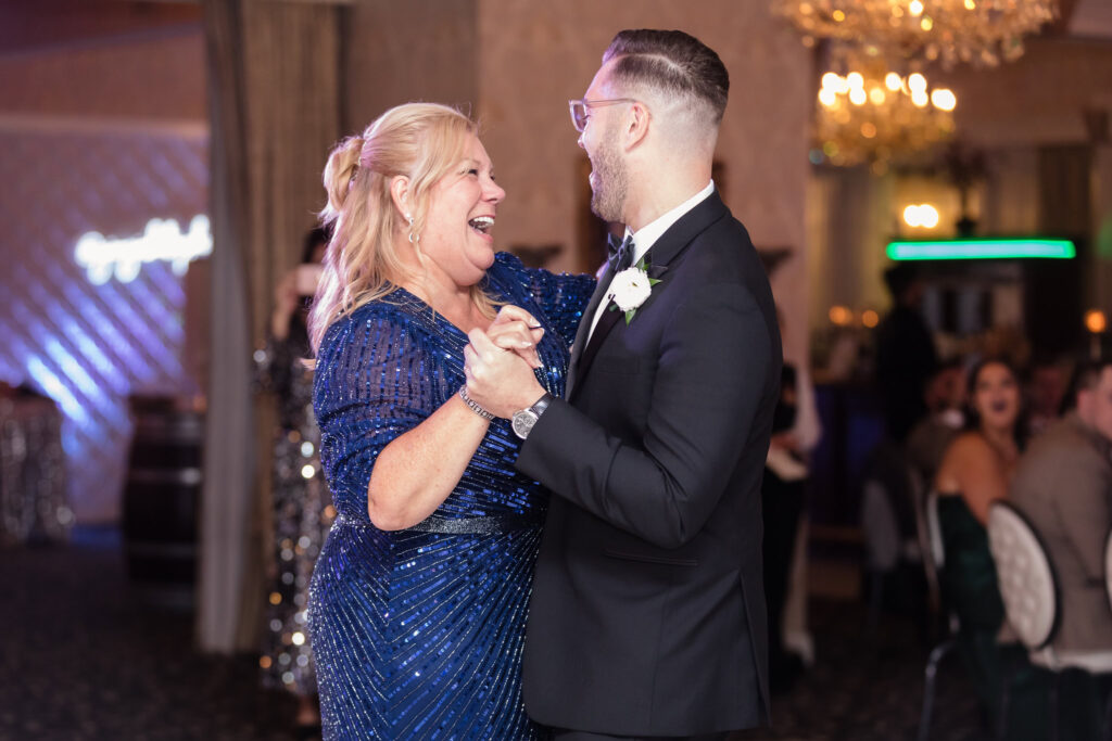 Groom Marc shares a joyful dance with his mother during the reception at Giorgio’s Baiting Hollow, both smiling warmly under the glow of the chandeliers.