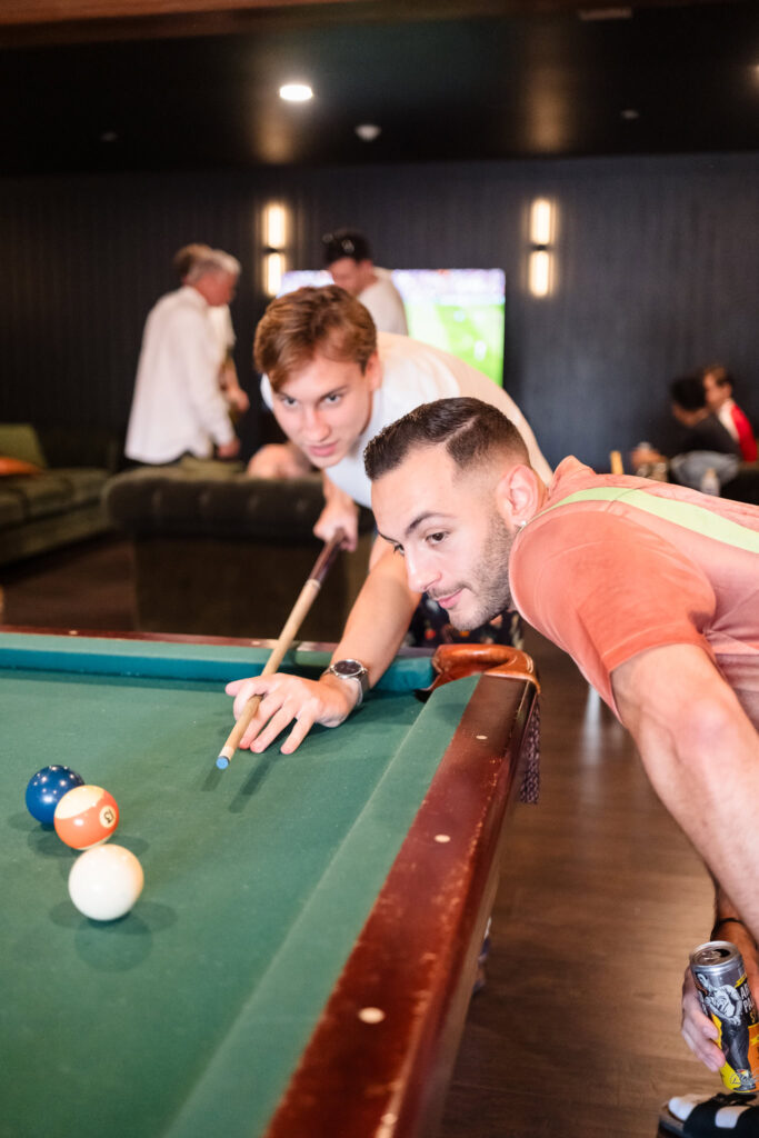 Groomsmen enjoy a relaxed moment playing pool inside the groom’s suite at Hiland Park Wedding Venue in Queensbury, NY, before the ceremony.