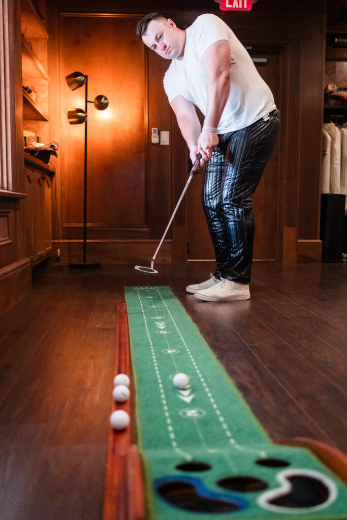 Groom practices putting on a mini indoor green in the groom’s suite at Hiland Park Wedding Venue, highlighting the country club’s golf-inspired charm in Upstate NY.