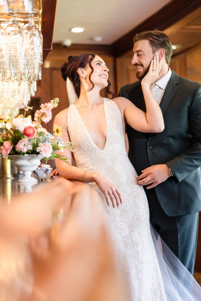 Bride and groom share a romantic moment at the bar inside Hiland Park Country Club, surrounded by soft lighting and elegant floral arrangements on their wedding day.