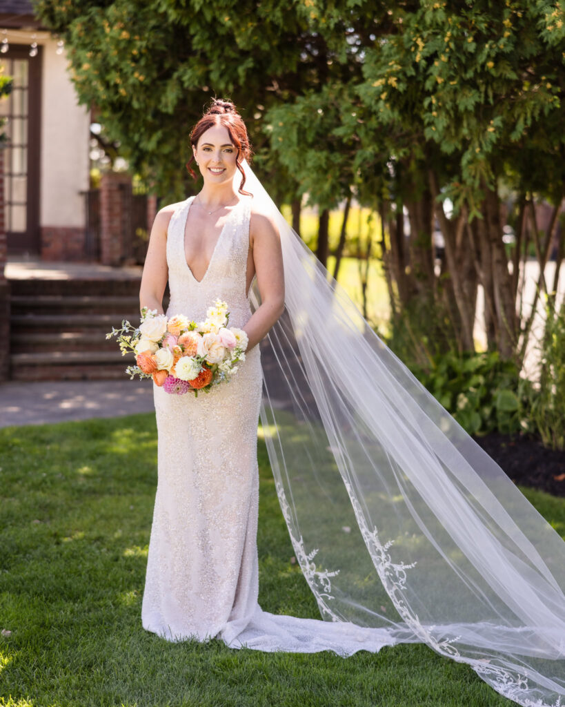 Bride poses with a vibrant bouquet and flowing veil in the gardens of Hiland Park Wedding Venue, showcasing her elegant gown and radiant smile.