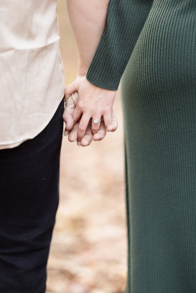 Close-up of couple holding hands during their engagement session, with the engagement ring softly framed against earthy fall tones and textured fabric.