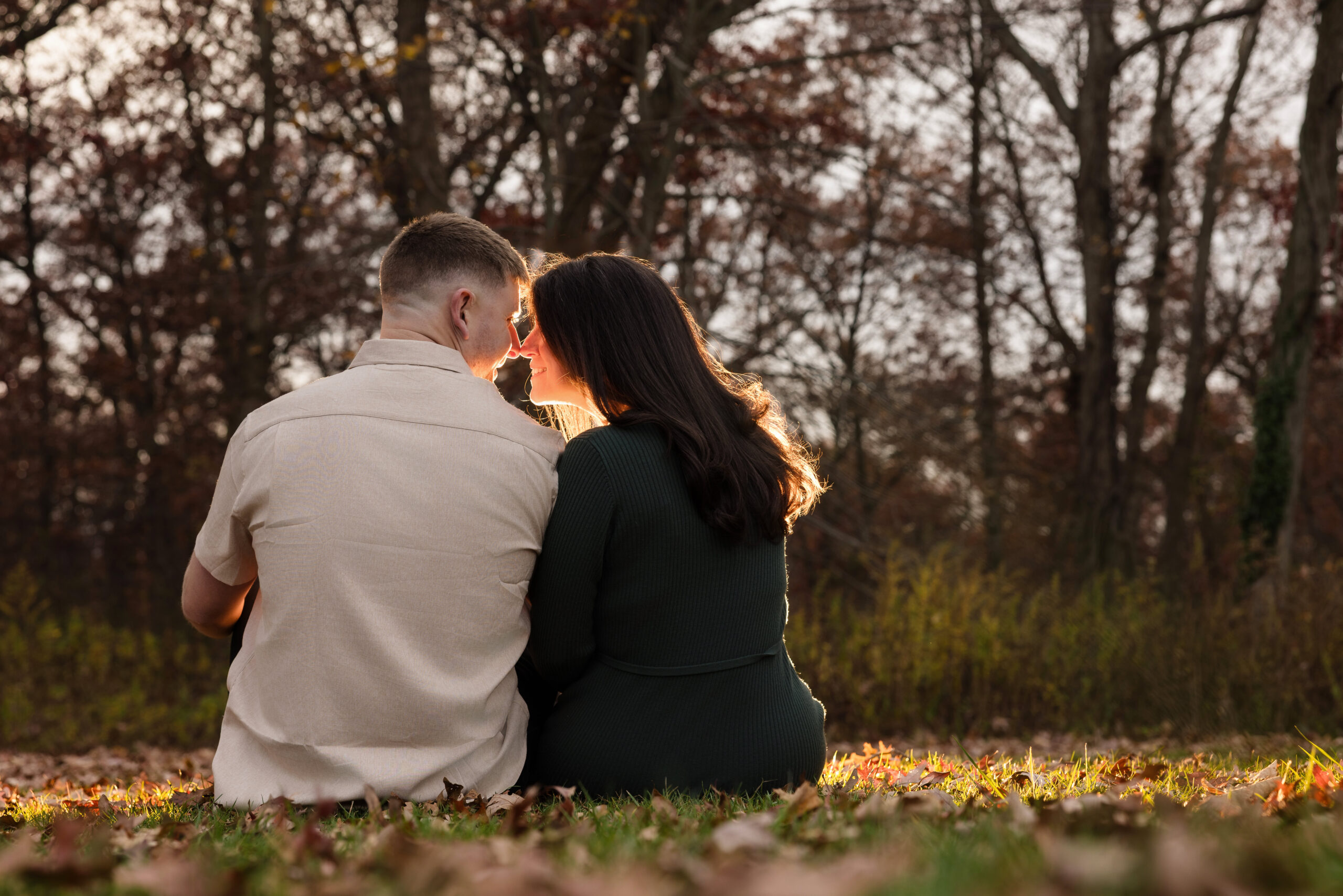 Couple sitting close in a quiet Bethpage field, softly backlit by golden autumn light a peaceful, intimate moment that reflects the stillness of late fall.