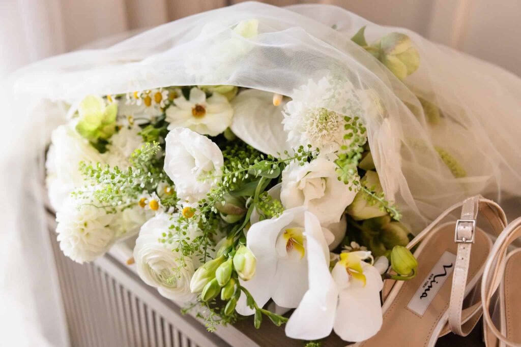 Elegant bridal bouquet of white orchids, ranunculus, and chamomile flowers, styled with a delicate veil and nude heels at Danfords Hotel before a summer wedding.