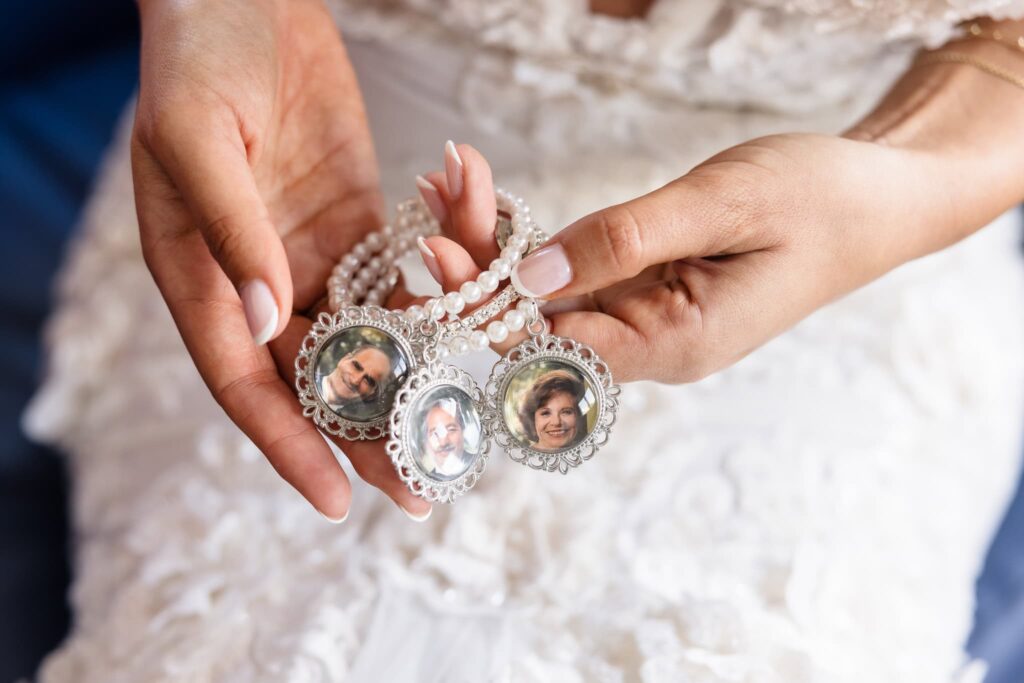 Bride holding a pearl bracelet adorned with photo charms honoring late loved ones, a meaningful heirloom tribute woven into her wedding day.