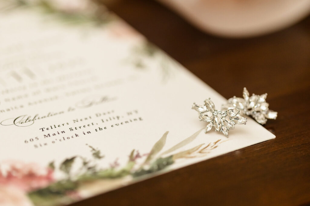 Close-up of wedding invitation for a Tellers Next Door wedding in Islip, NY, paired with elegant crystal bridal earrings for a refined flat lay detail.