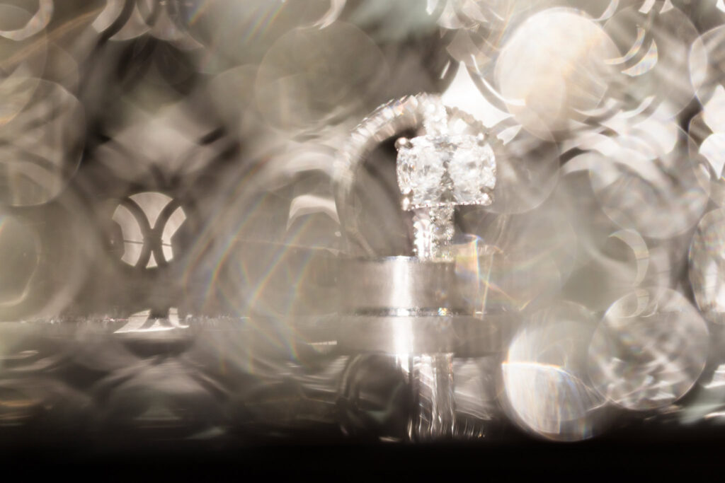 Creative macro shot of wedding rings with cushion-cut diamond engagement ring surrounded by abstract bokeh reflections at Tellers Next Door wedding.