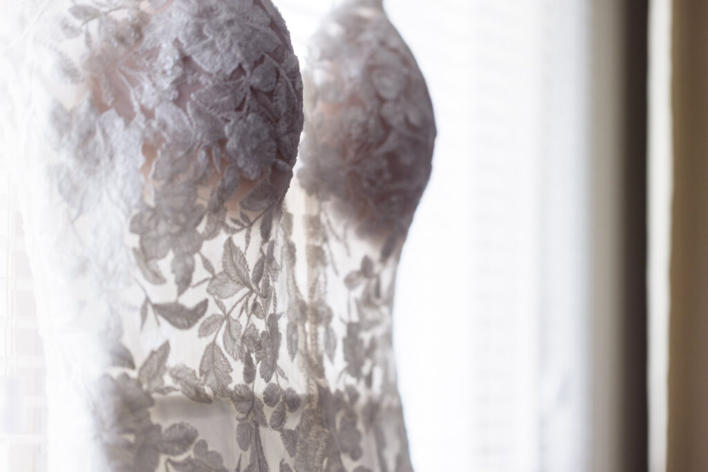 Close-up of lace floral details on bridal gown hanging near window, showcasing intricate design before elegant Tellers Next Door wedding.