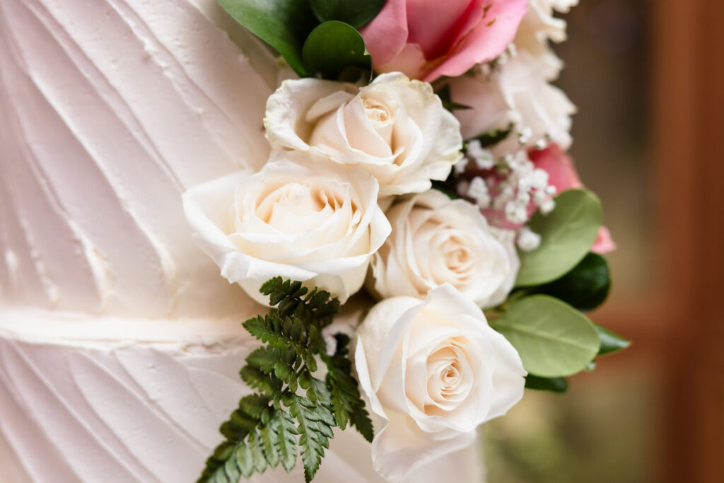 Close-up of delicate ivory and blush roses with greenery embellishing a white tiered wedding cake.