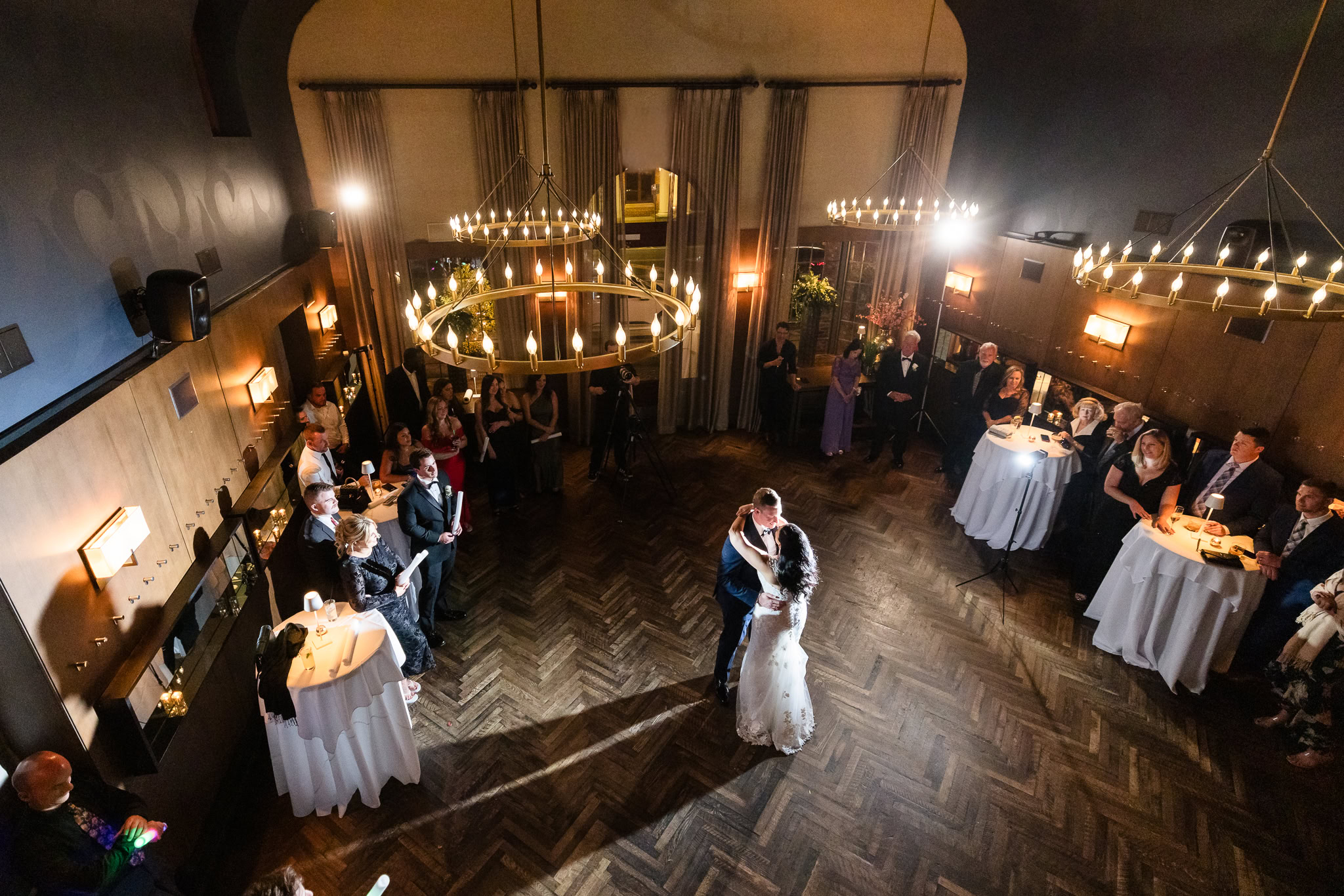 Bride and groom share their first dance under elegant chandeliers at Tellers Next Door, surrounded by guests in a warm, intimate reception setting.