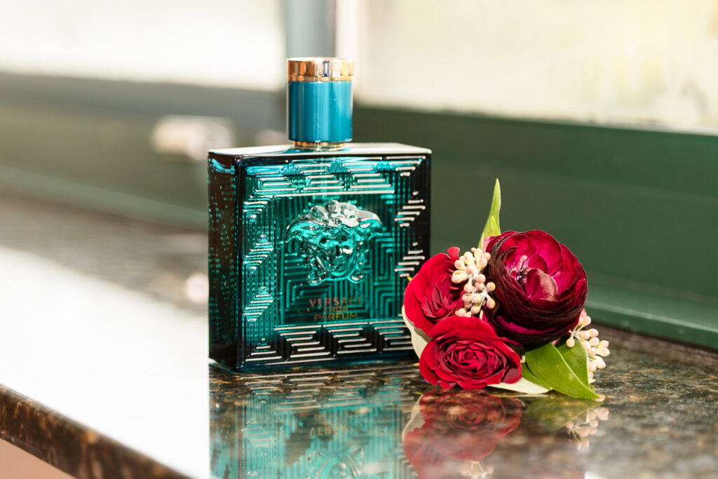 Versace Eros cologne styled with a deep red boutonniere on a marble countertop, highlighting refined groom’s details.