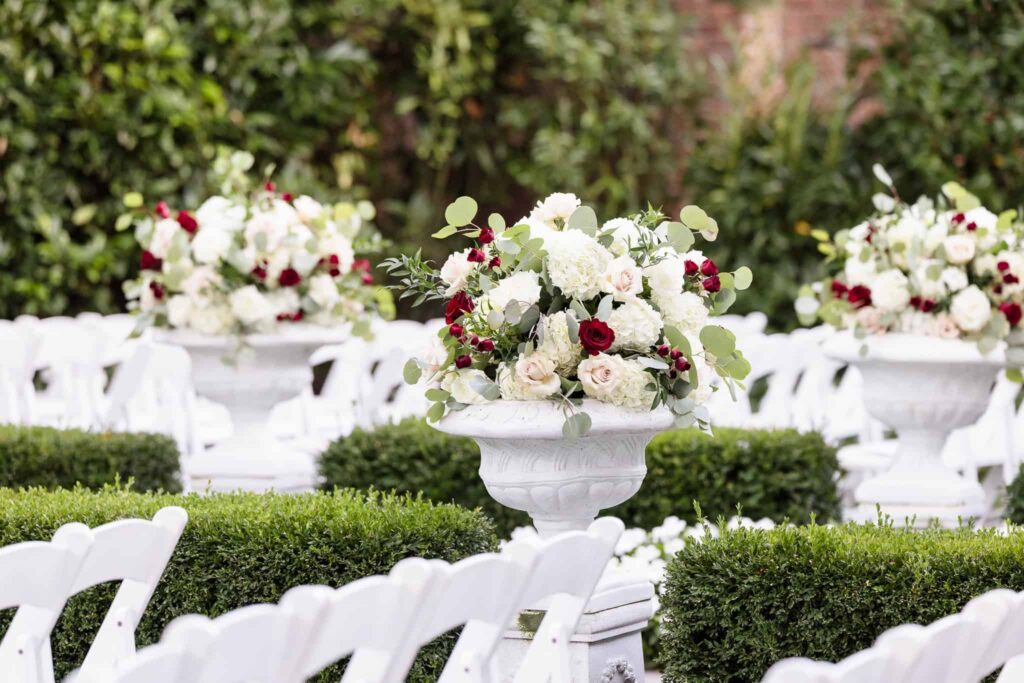 Elegant floral urns filled with white hydrangeas, blush roses, and deep red blooms line the garden ceremony aisle at Westbury Manor, creating a classic and romantic outdoor wedding setting.