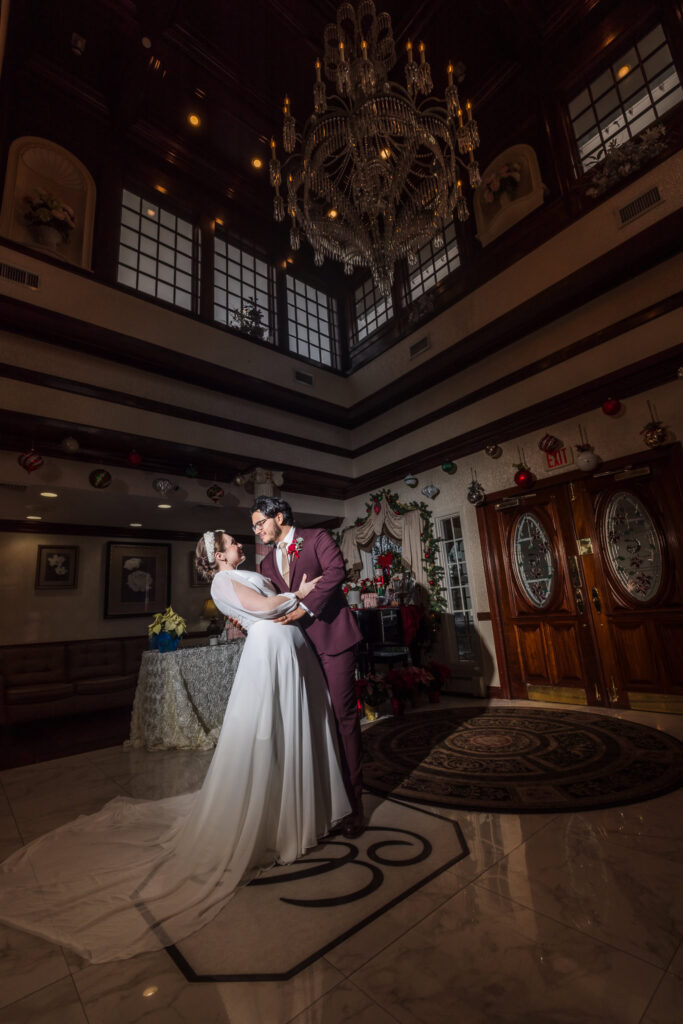 Bride and groom share a romantic dip under the grand chandelier in the lobby of Giorgio’s Baiting Hollow, surrounded by festive holiday decor.