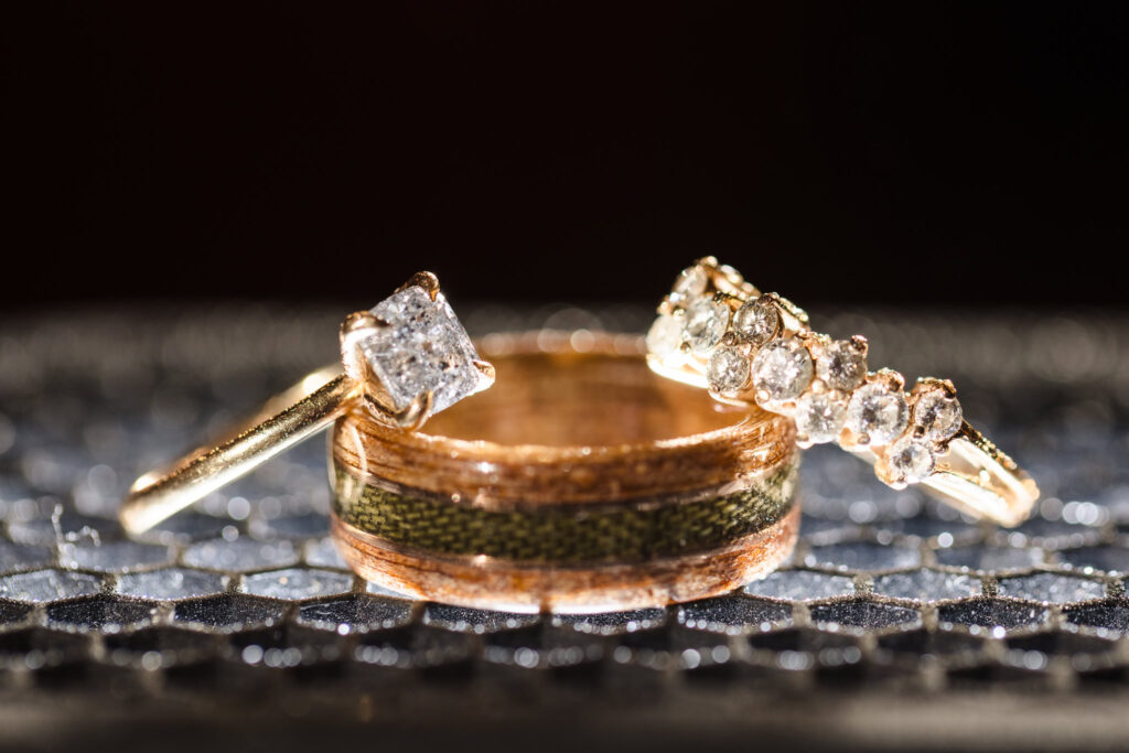 Artistic close-up of gold wedding rings and diamond engagement ring displayed on a shimmering surface at a wedding.