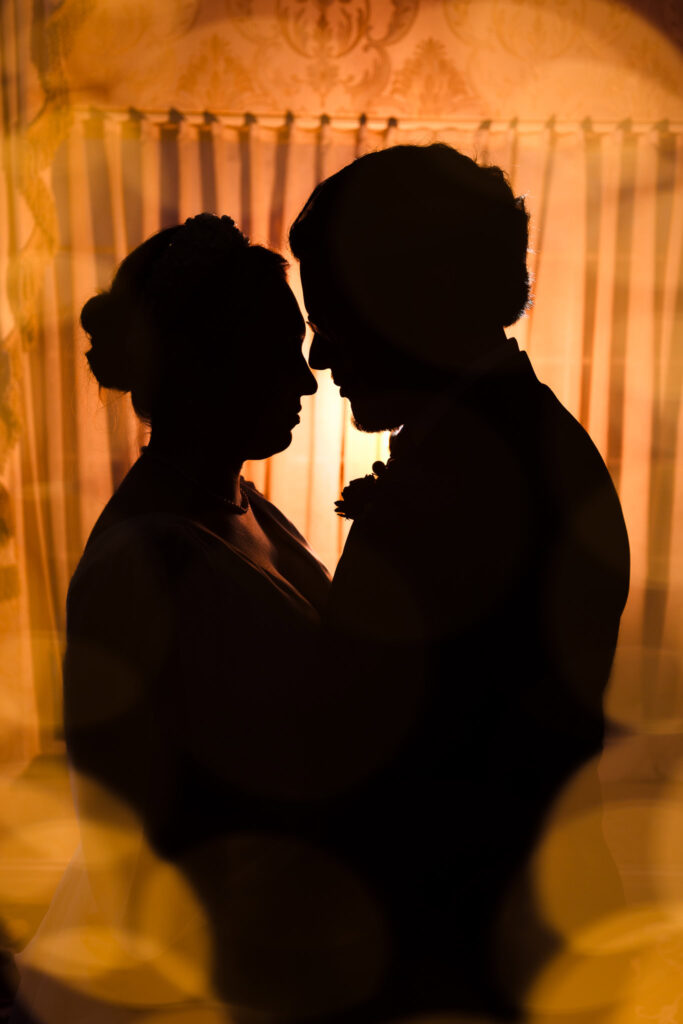Silhouetted portrait of bride and groom in an intimate embrace with golden bokeh and warm backlighting during their winter wedding.