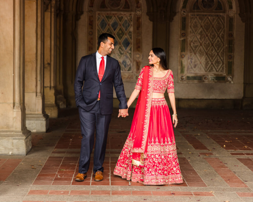 Engaged couple walking hand in hand through Bethesda Terrace during their Central Park engagement session with South Asian attire.