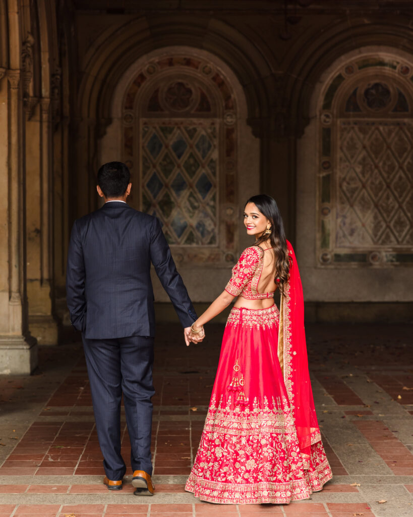 Bride-to-be smiling back at the camera while holding hands with her fiancé at Bethesda Terrace during their NYC South Asian engagement session.