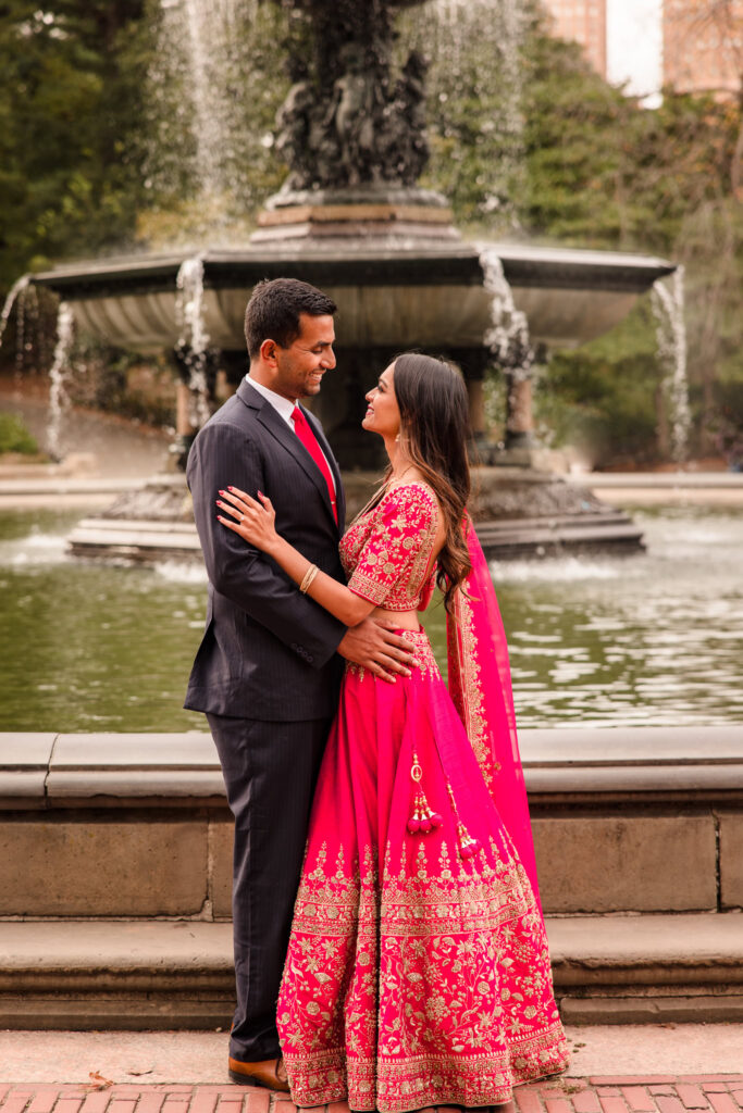 South Asian couple gazing at each other in front of Bethesda Fountain during their Central Park engagement session in traditional Indian attire.